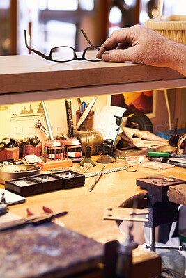 Buy stock photo Cropped view of a craftsman reaching for his glasses at his workstation