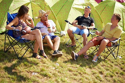 Buy stock photo Camping, group of friends in conversation at tent and relax with outdoor chat, drinks and grass. Nature, men and woman at campsite together for music festival, adventure and people bonding in park.