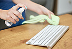 Hands, keyboard and spray bottle with a person cleaning a keyboard on a wooden desk for hygiene. Technology, health and sanitize with an adult wiping a wireless device on a table