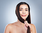 Portrait of a beautiful mixed race woman with clean skin and healthy brown hair posing against a studio background. Woman pulling on her hair to show its strength and showing no breakage