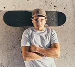 Skateboard, fashion or man with arms crossed in city skate park for stunt training, hobby exercise or freestyle skating in top view. Portrait, skater or skateboarder lying on concrete ground or floor