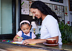 Drawing, learning and girl with mother at cafe with books, studying and art education. Family care, love and mama teaching kid how to color with crayons, having fun and bonding together in restaurant