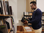 Librarian man, shelf and book with thinking, packing or stock for admin, organized and ideas in workplace. African employee, university or library expert with research, book and reading at workplace