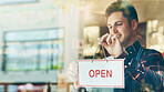 Open, sign and man at window of restaurant for hospitality, information and start of service. Coffee shop, smile and waiter with board by glass for small business, message and beginning of work day