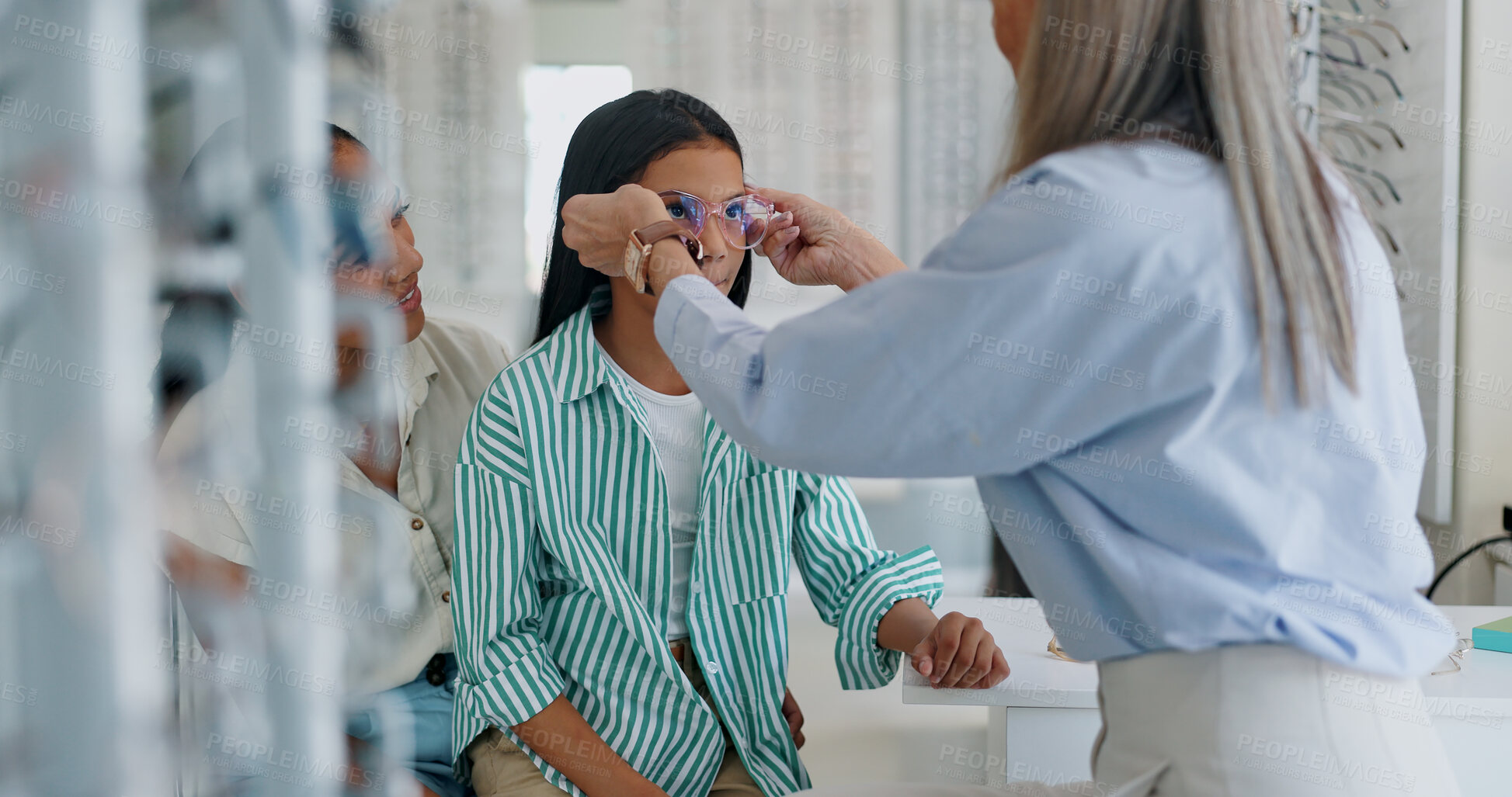 Buy stock photo Mother, child and glasses with optometrist for sight, vision or eye care at retail, shop or store. Mom, daughter and mature optician helping customer try on spectacles for size, decision or choice