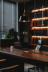 Office, design and dark interior with desk, laptop and empty or table in modern workspace in business. Productivity, room and lights for professional work, chair and plant with nobody or furniture