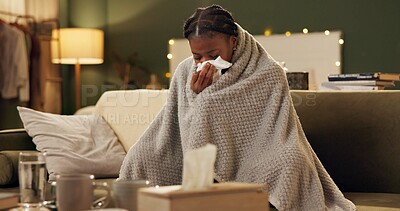 Woman, cold and tissue with blanket on sofa for blowing nose, recovery or winter virus in living room. African person, infection or sick with fever, sinus and allergy on couch in home with healthcare