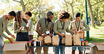 Happy people, volunteer and packing with bags for charity, food and community service at outdoor park. Group or team working together in NGO with resources, supplies or mission for future in need