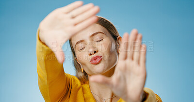 Buy stock photo Woman, finger and frame with happy kiss or emoji face,  photographer perspective for social media post or picture. Blue background, hand gesture and cosmetic beauty, glow and confident for capture