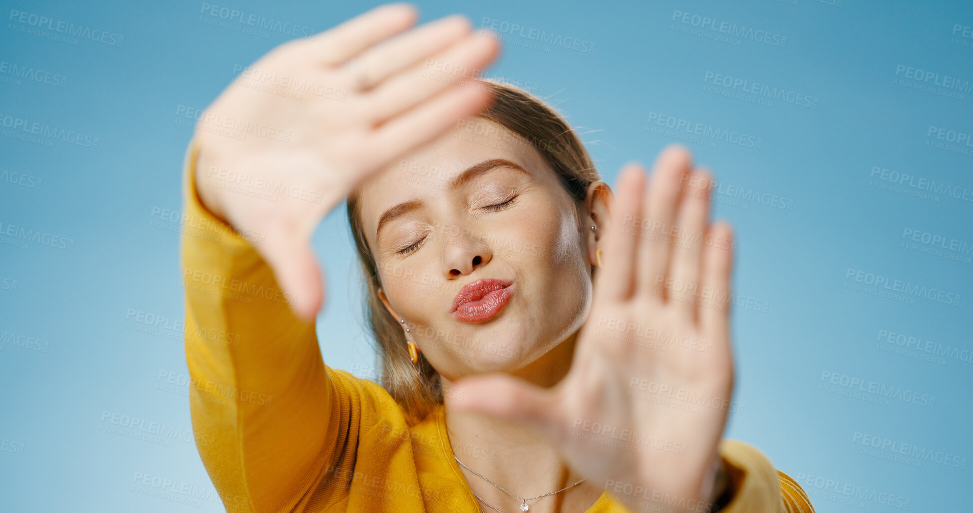 Buy stock photo Woman, finger and frame with happy kiss or emoji face,  photographer perspective for social media post or picture. Blue background, hand gesture and cosmetic beauty, glow and confident for capture