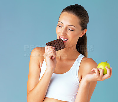 Buy stock photo Apple, woman and chocolate choice in studio for health, food and diet plan in isolated blue background. Smile, green fruit and face of young vegetarian person for detox, vegan or decision