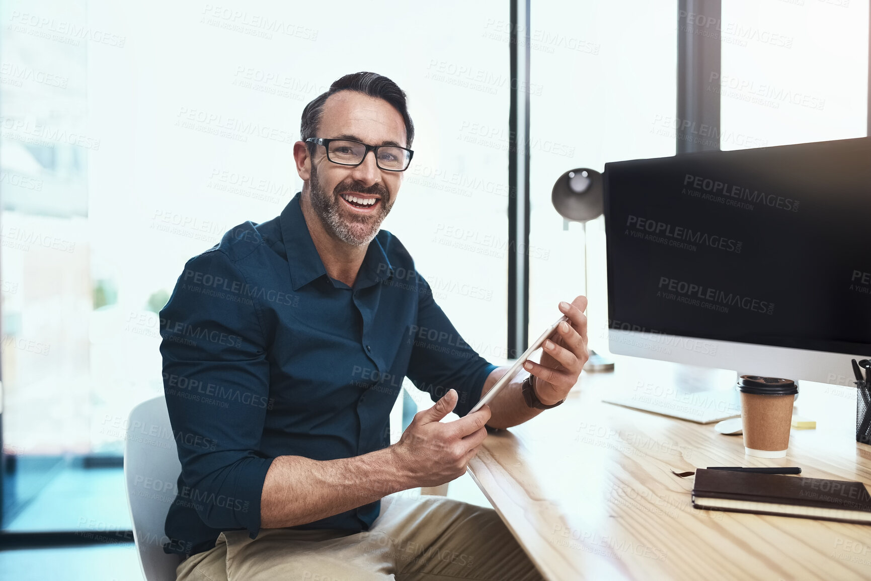 Buy stock photo Shot of a mature businessman using his digital tablet while sitting at his desk