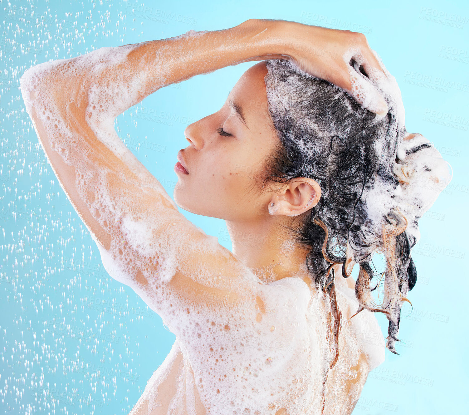 Buy stock photo Wash, hair care and woman shower in studio for hygiene, shampoo or skincare on blue background. Back, wellness and model body with water splash for morning routine, cleaning foam or dermatology