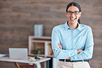 Portrait of a young happy cheerful mixed race businesswoman wearing her spectacles smiling while standing with her arms crossed alone in an office at work. One hispanic female boss standing while working at a startup company 
