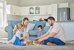 Happy caucasian family of four smiling while playing with toys and sitting on the floor together in the lounge at home. Two loving parents spending time with their little carefree son and daughter