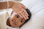 Closeup shot of a cute mixed race little boy feeling unwell and looking while lying in bed at home. Young mother feeling the temperature of her sick child while lying on a sofa 