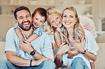 Portrait of smiling caucasian family relaxing together on a sofa at home. Carefree playful little son and daughter hugging arms around loving parents. Happy kids bonding with mom and dad