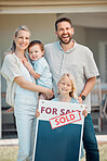 Portrait of happy caucasian family holding for sale and sold sign while relocating and moving in new house. Smiling parents and kids securing homeowner loan for property real estate and home purchase