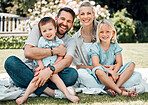 Portrait of a caucasian family sitting on a blanket in the backyard on a sunny day smiling. Parents sitting with cute little son and daughter enjoying time together