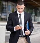 A handsome young mixed race business man using his cellphone while walking through the city on his way to work. Young and confident corporate professional checking messages during his morning commute
