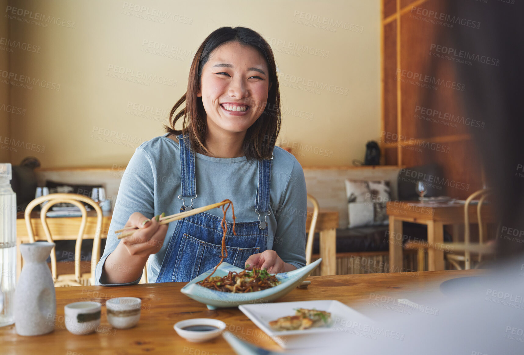 Buy stock photo Japanese, food and woman at a restaurant eating for dinner or lunch meal using chopsticks and feeling happy with smile. Plate, date and person enjoy Asian cuisine, noodles or diet at a table