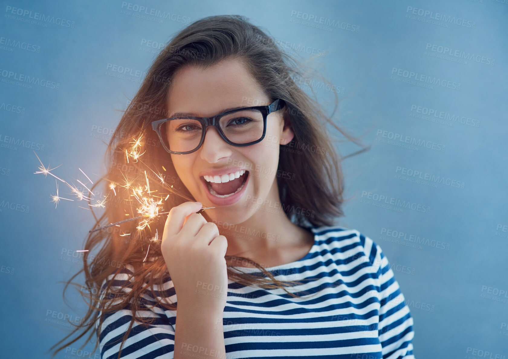 Buy stock photo Studio, portrait and happy woman with sparklers for light with celebration isolated on blue background. Glasses, smile and new years party or fun birthday event with confidence, glow and fireworks.