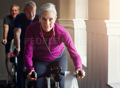 Buy stock photo Woman, riding and bike for fitness with earphone at gym spin class, training and workout listening to music for inspiration. Senior female, cycling machine and exercise performance for cardio health