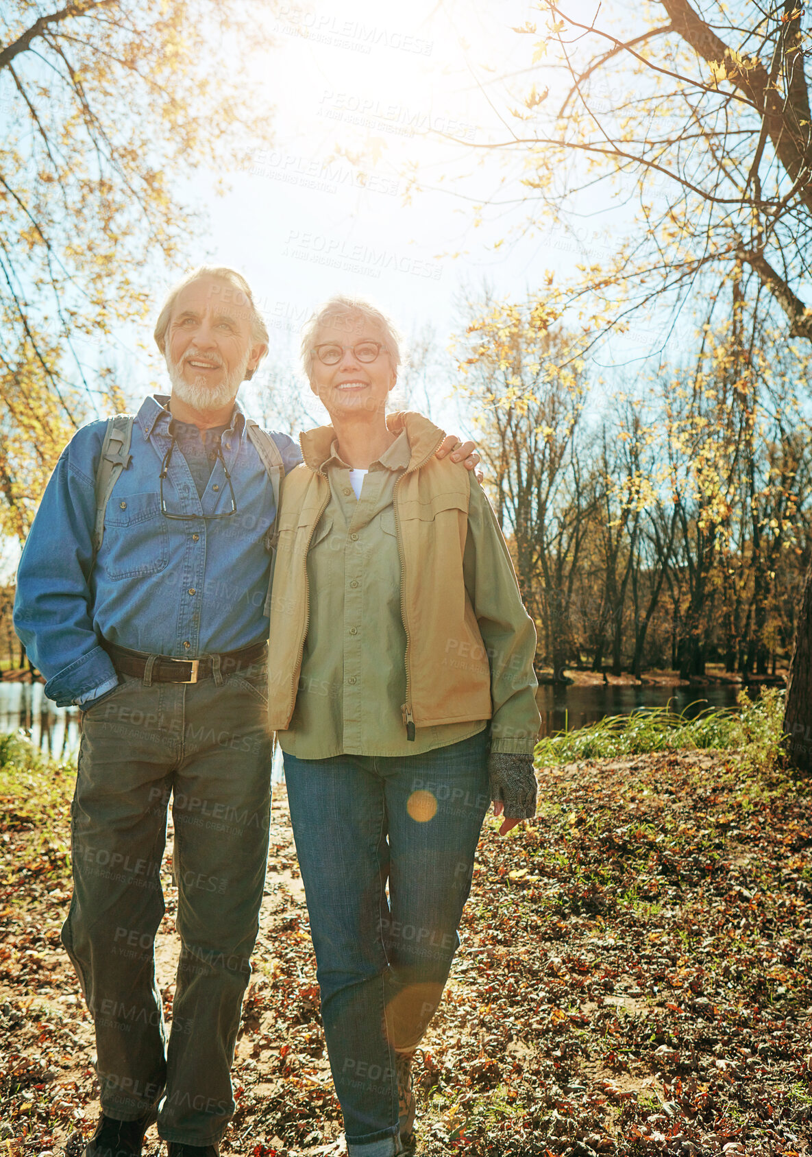 Buy stock photo Happy, nature and senior couple in forest with backpack for walk, exercise and bonding together. Smile, love and elderly man and woman in retirement enjoying view by woods in Autumn in England.