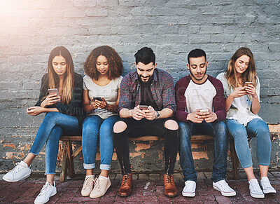 Buy stock photo Students, row and outdoor with smartphone on bench for study break, social media and campus friends. University, people and online with technology for communication, wall background and relax