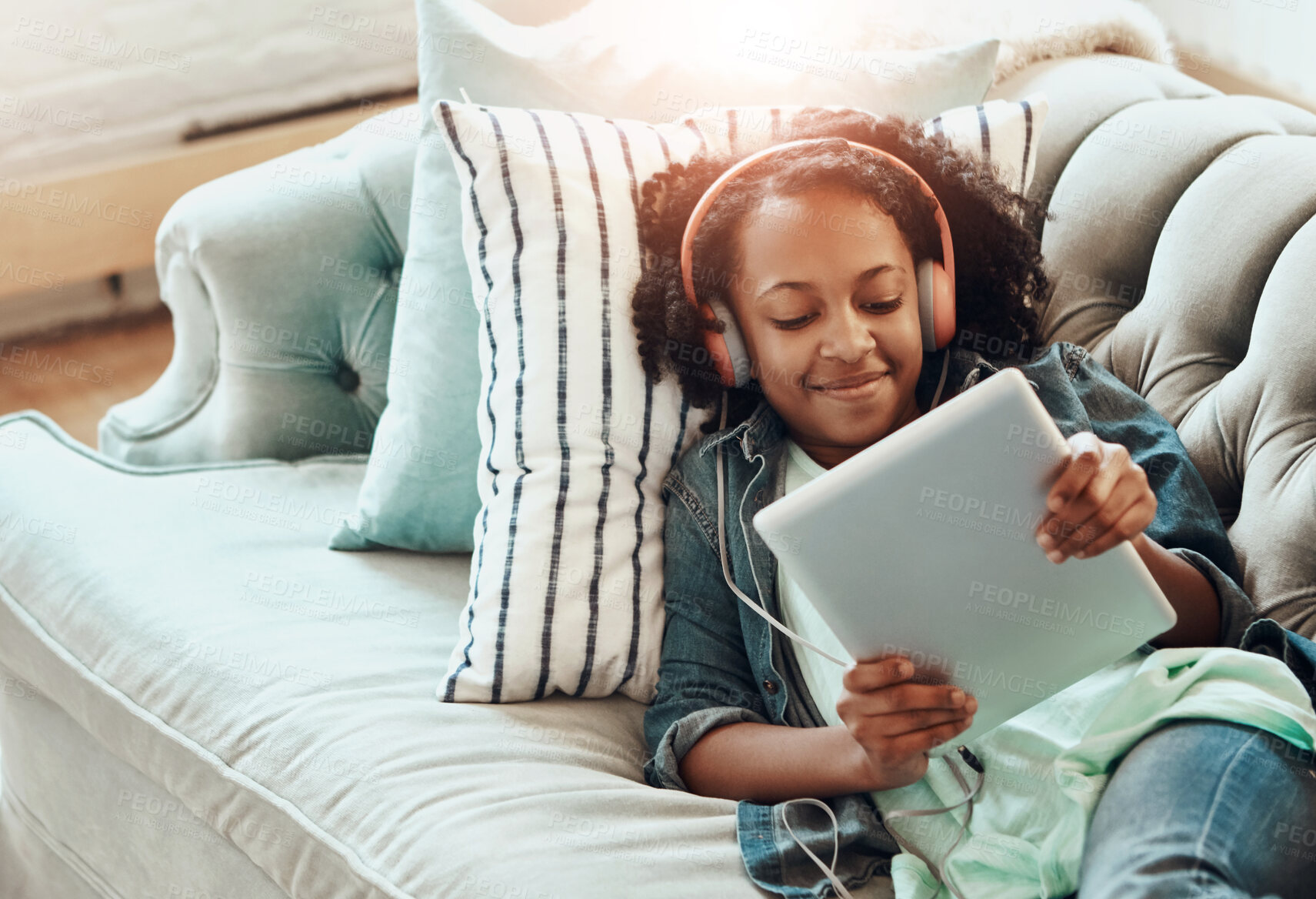 Buy stock photo Happy girl, headphones and watching with tablet on sofa for online streaming, music or entertainment at home. Young female person, child or student in relax with smile for technology, audio or sound