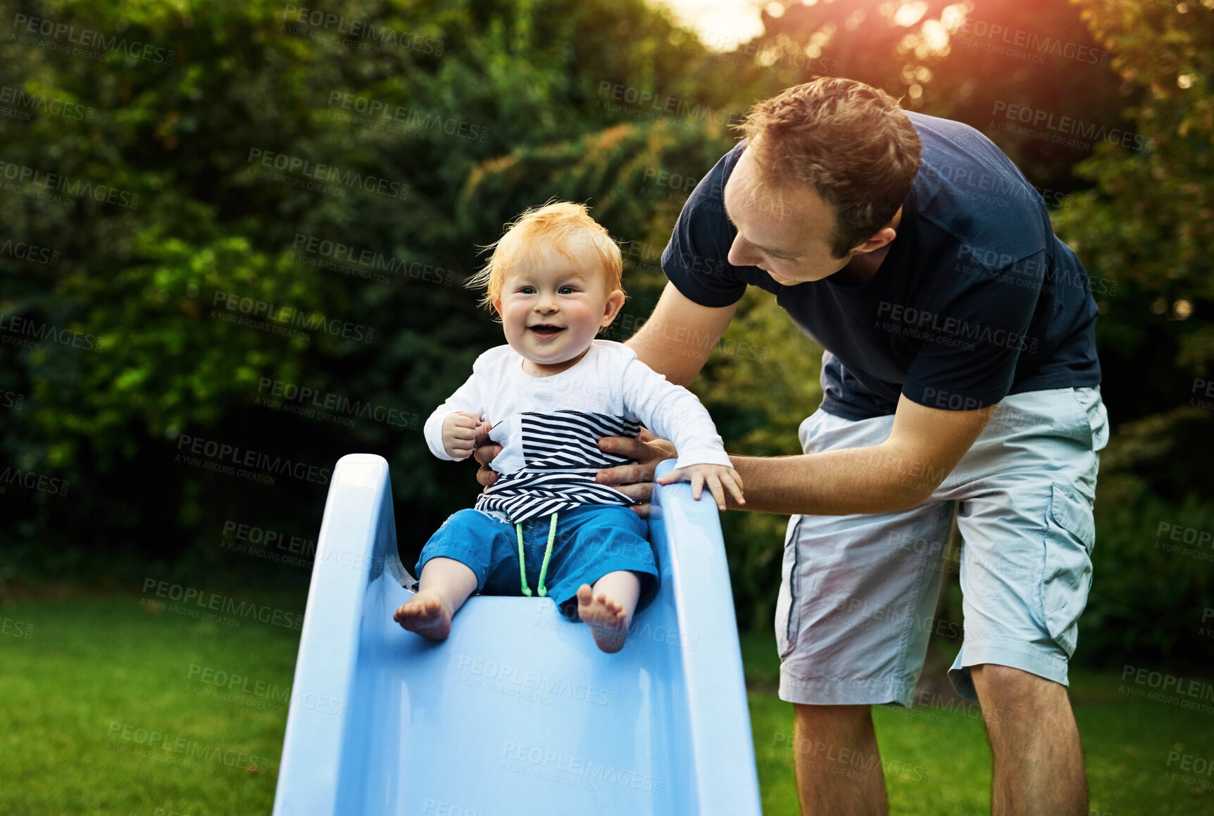 Buy stock photo Man, baby boy and garden slide for fun, growth and development with support in backyard. Male person, park and help for toddler on plastic ride with learning, happiness together and healthy bonding