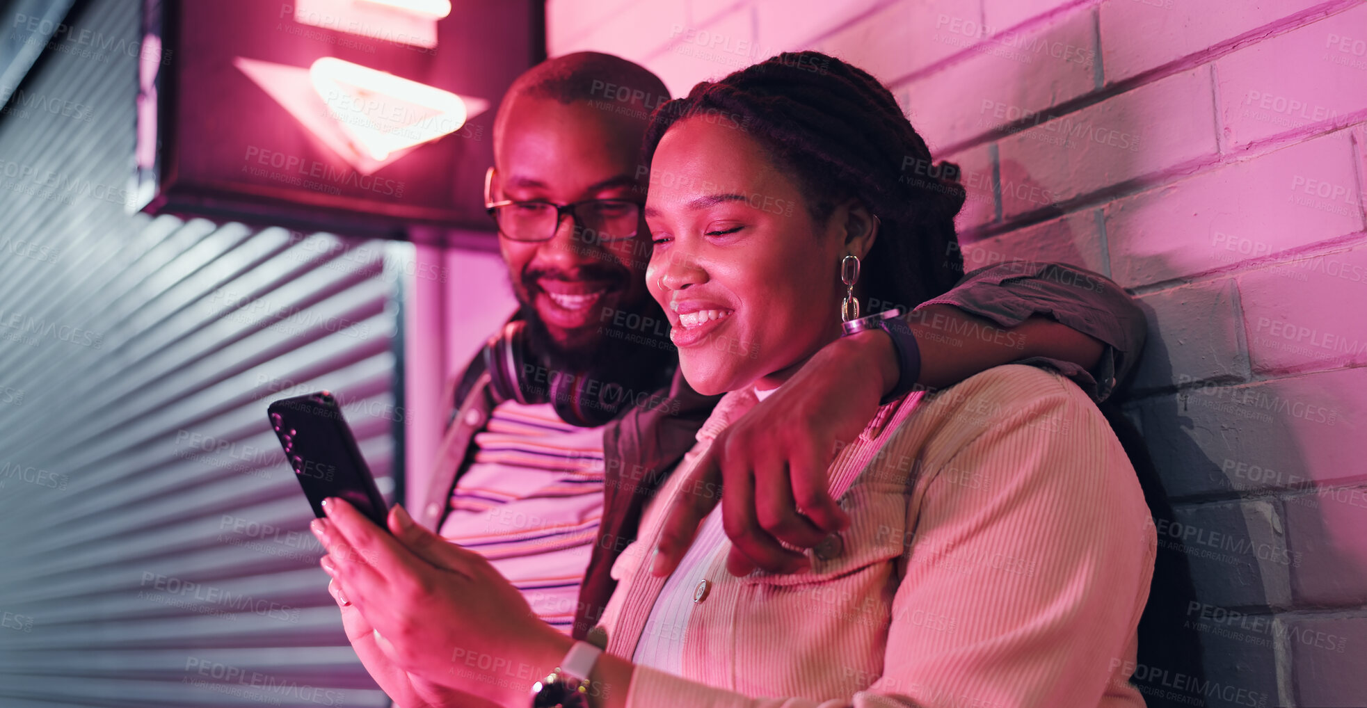 Buy stock photo Date, phone and smile with black couple by neon light in city at night together for ride, love or romance. App, communication or social media with man and woman outdoor in urban town for evening