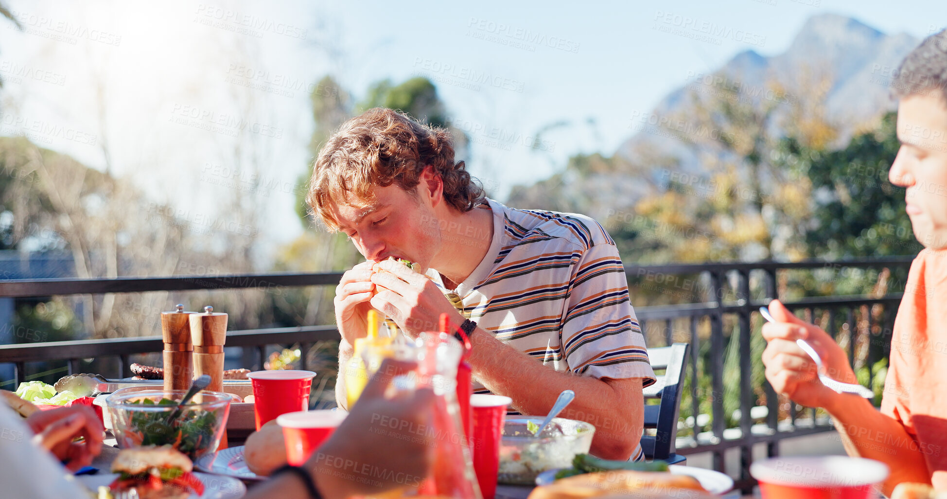 Buy stock photo Friends, man and eating hamburger outdoor on terrace with hunger, reunion and social event in summer. People, barbecue and lunch on patio with food, feast or celebration with bonding and drinks