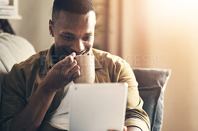 Buy stock photo Cropped shot of a handsome young man drinking coffee while using a digital tablet in his living room at home