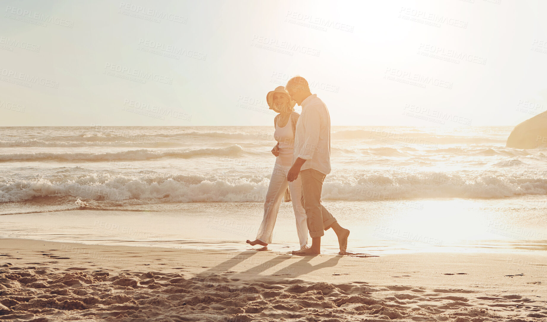 Buy stock photo Full length shot of an affectionate middle aged couple walking hand in hand along the beach at sunset