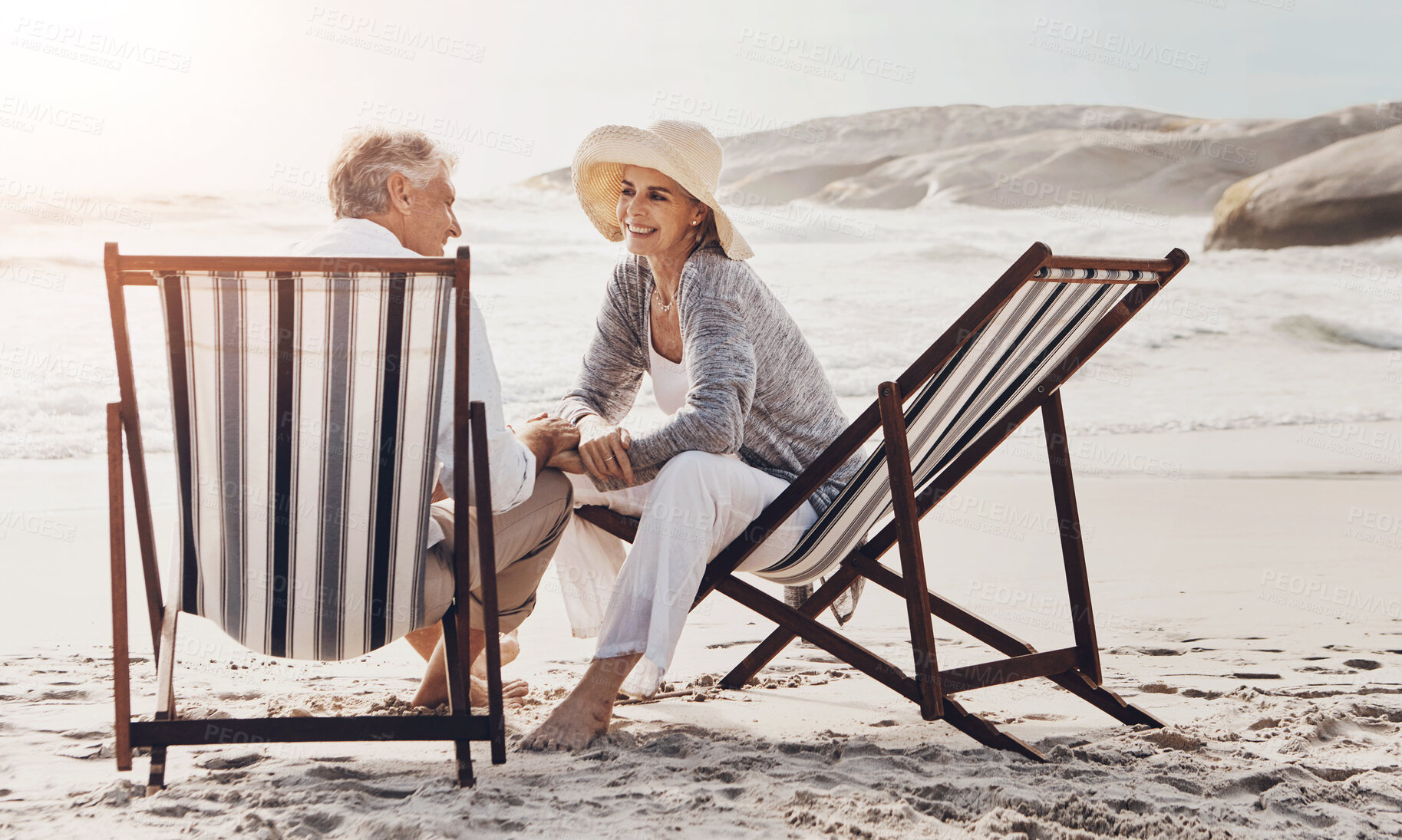 Buy stock photo Full length shot of an affectionate middle aged couple relaxing on loungers at the beach