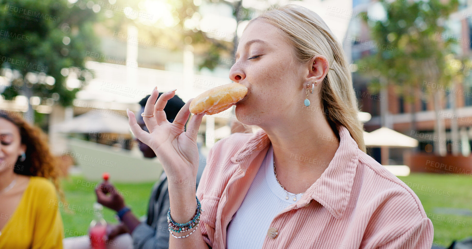 Buy stock photo Friends, woman and eating at university picnic with donut and happy from party at campus park. College, lunch and student with dessert on garden and lawn with Gen Z people outdoor with food in group