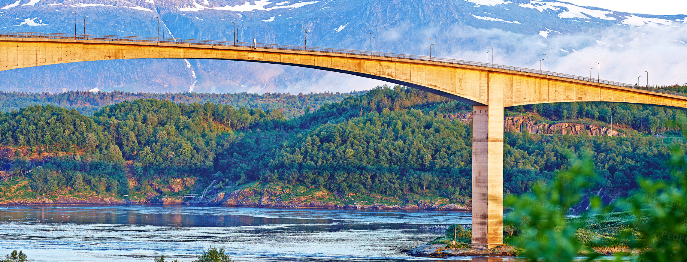 Buy stock photo Bridge, road and river with snow on mountains, nature and trees for travel in forest. Landscape, woods and hill with highway, infrastructure and transportation in environment with summer in Norway