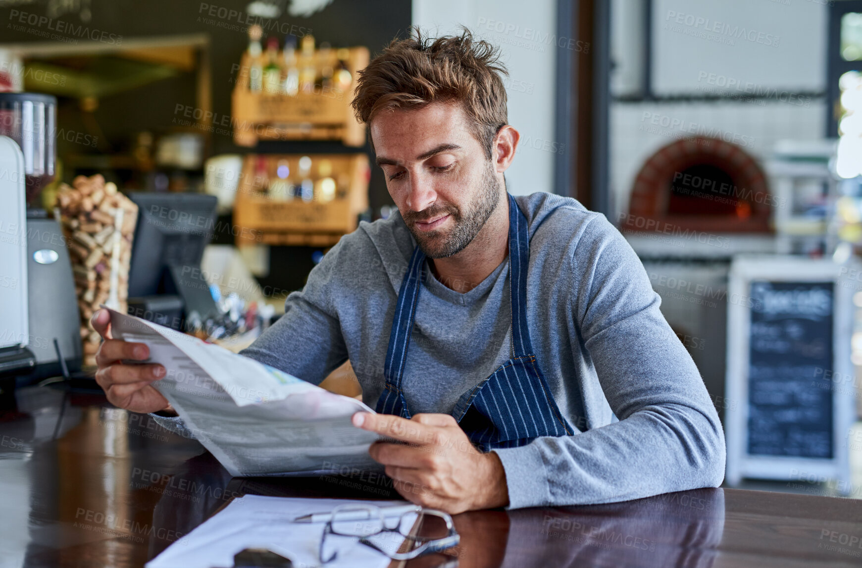 Buy stock photo Small business, cafe and man at table with newspaper, paperwork and relax in coffee shop. Reading, working and restaurant manager, waiter or owner checking news for service industry startup economy
