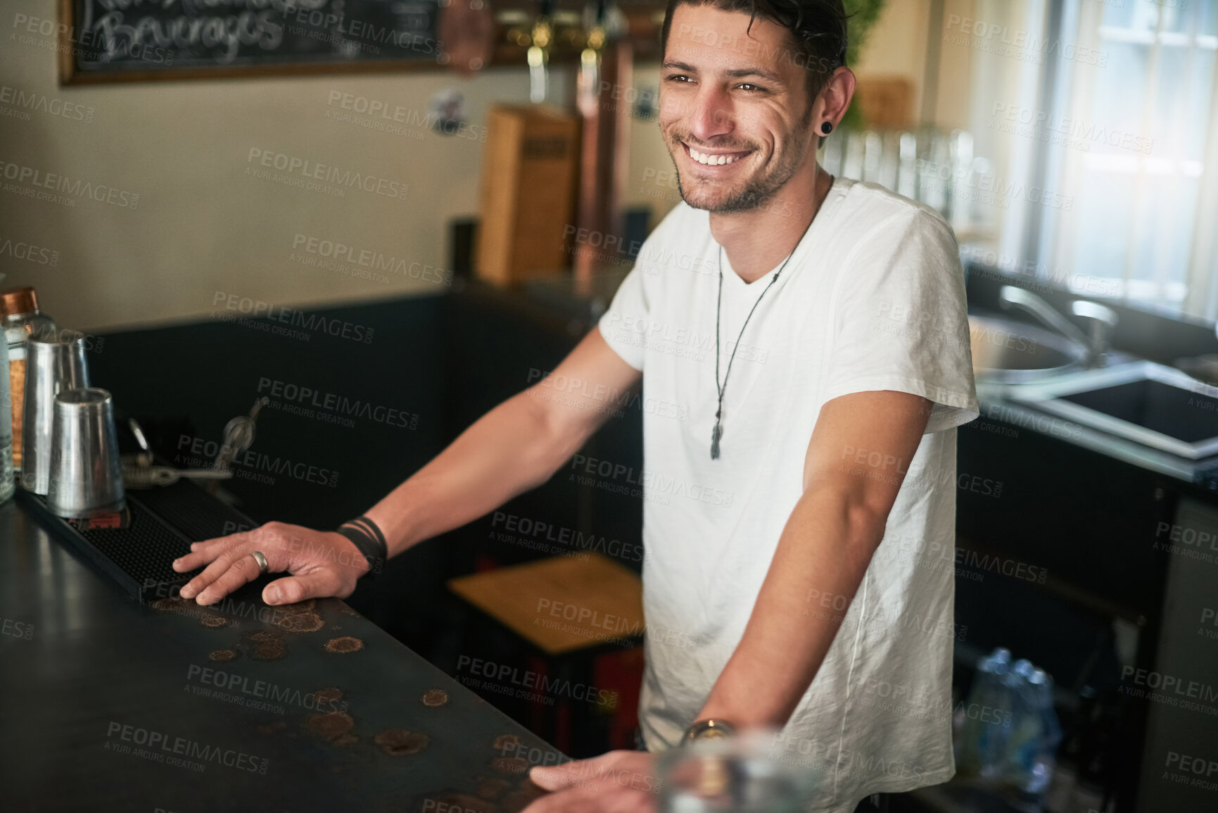 Buy stock photo Bartender, counter and smile with man in pub for friendly hospitality or service at small business. Cafe, restaurant or tavern and happy waiter person with tattoo at work as startup employee