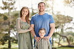 Young happy caucasian family relaxing and standing  together in nature. Loving parents spending time with their little son at the park. Carefree child bonding with mom and dad