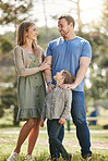 Young happy caucasian family relaxing and standing  together in nature. Loving parents spending time with their little son at the park. Carefree child bonding with mom and dad