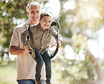 Excited little caucasian boy having fun while sitting in swing and being pushed by his grandfather at the park. Active senior man bonding and playing with adorable grandson outdoors