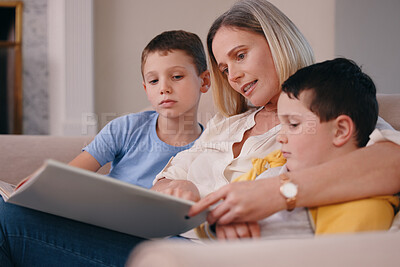 Buy stock photo Shot of a mother reading a book to her sons at home on the couch