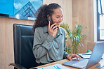 Young happy mixed race businesswoman on a call using a phone and working on a laptop sitting at a desk in an office at work. One hispanic female typing an email and talking on the phone