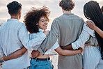 Rear view of a Unknown group of friends enjoying their time together at the beach. Diverse group of friends huddling outdoors