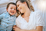 Above view of smiling caucasian mother lying in bed at home and bonding with her adorable little son. Happy cute cheerful boy laughing with his single parent. Beautiful woman together with her child