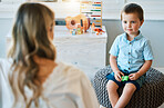 An adorable little boy sitting in his bedroom at home and talking to his mother. Happy male child bonding with his mom. Rearview of a blonde woman spending quality time with her young son on a weekend