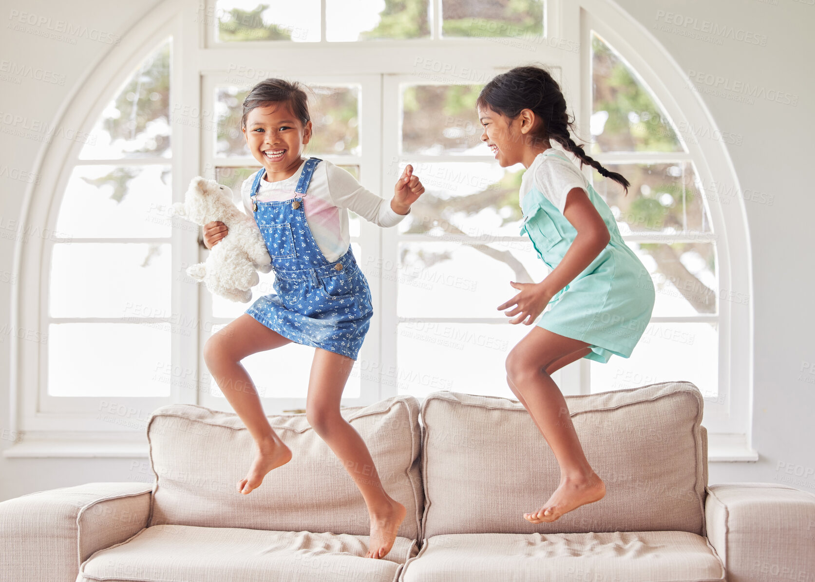 Buy stock photo Girl, children and sisters with jump on sofa, portrait and happy with bonding, dance or game in house. Kids, excited and smile with love, connection and toys on couch in living room at family home