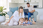 Family enjoying a movie together. A happy young family looking at a tablet together while lying on the carpet in their lounge while their father uses a laptop
